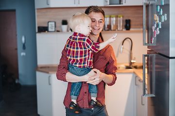 Isä pitelee pientä poikaansa sylissään, joka tutkii jääkaapin oveen kiinnitettyjä magneetteja