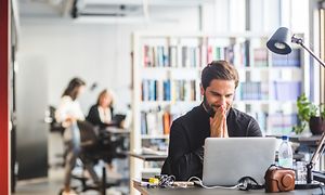 Mies istuu miettimässä kannettavan äärellä toimistossa