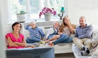 Viisihenkinen perhe istuu sohvalla katselemassa televisiota