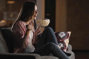 Nuori nainen istuu sohvalla katsomassa televisiota popcorn-kulho kädessään