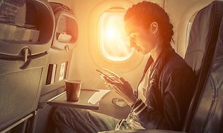 Lentokoneessa istuva nainen käyttää älypuhelintaan