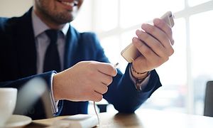 Pukuun pukeutunut, hymyilevä mies laittaa älypuhelintaan lataukseen powerbank-varavirtalähteeseen