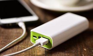 Kahvilan pöydällä, kahvikupin vieressä oleva älypuhelin latauksessa powerbankin avulla