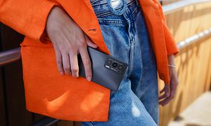 Oranssiin takkiin ja farkkuihin pukeutunut nainen pitelee Motorola Edge 20 -puhelinta kädessään