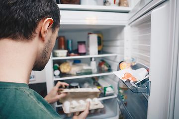 Mies katsoo kananmunapakettia avoimessa jääkaapissa