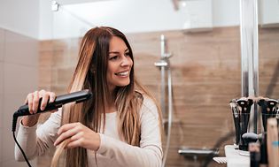 Nainen käyttää suoristusrautaa hiustensa muotoilemiseen