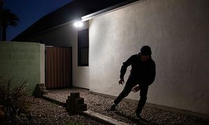 Tummiin pukeutunut henkilö hiiviskelee talon ulkopuolella