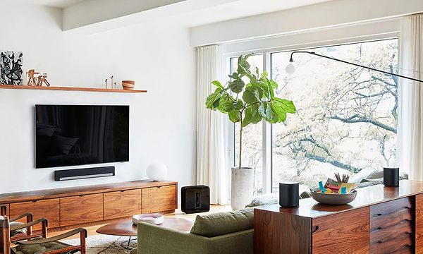 Moderni olohuone, jossa seinälle kiinnitetty tv, soundbar-kaiutin ja erilaisia älykaiuttimia ympäri huonetta
