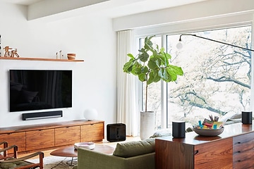 Moderni olohuone, jossa seinälle kiinnitetty tv, soundbar-kaiutin ja erilaisia älykaiuttimia ympäri huonetta