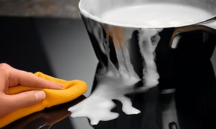 Electrolux-induktioliesi sekä käsi puhdistamassa keittotasoa