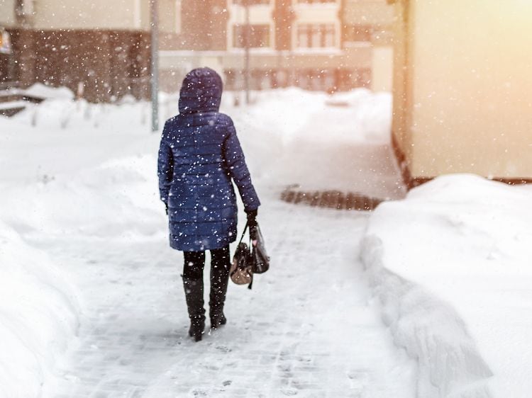 Siniseen takkiin pukeutunut nainen kävelee lumisessa kaupungissa lumisateella