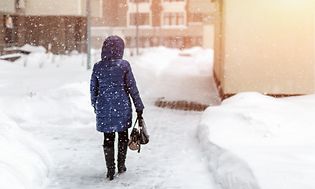 Siniseen takkiin pukeutunut nainen kävelee lumisessa kaupungissa lumisateella