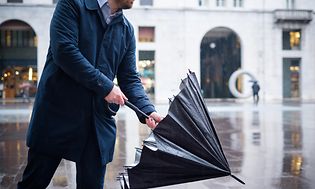 Siniseen takkiin pukeutunut liikemies avaa sateenvarjoaan