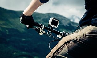 Mies seisoo pyöränsä kanssa vuoristomaisemassa, action-kamera ohjaustankoon kiinnitettynä