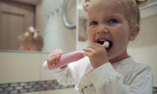 Pieni lapsi harjaa hampaitaan sähköhammasharjalla kylpyhuoneessa