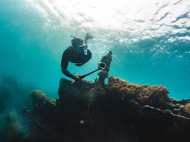 Mies sukeltaa koralliriutalla ja kuvaa vedenalaista maailmaa GoPro-kameralla