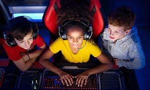 Kolme kouluikäistä lasta pelaavat yhdessä tietokoneella