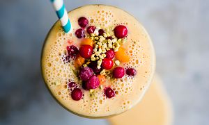 Oranssi, marjoilla koristeltu smoothie ja pilli lasissa