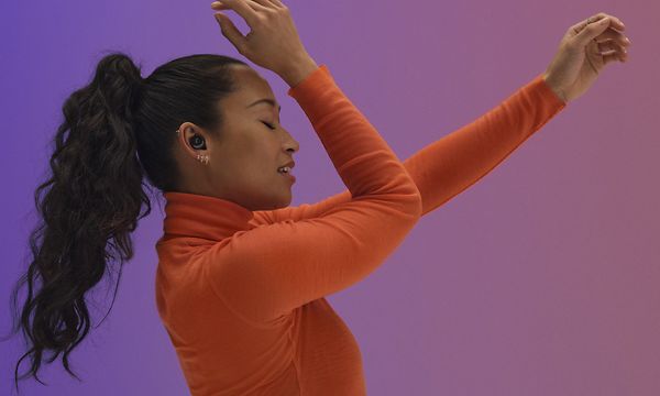 Oranssiin paitaan pukeutunut nainen kuuntelee musiikkia Sennheiser Momentum TW3 -kuulokkeilla