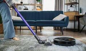 Ihminen imuroi mattoa varsi-imurilla ja vieressä on robottipölynimuri