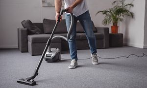 Mies imuroi olohuonetta harmaalla johdolliselle pölynimurilla