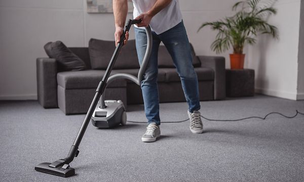 Mies imuroi olohuonetta harmaalla johdolliselle pölynimurilla