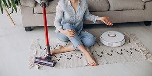 Nainen istuu lattialla vieressään Dyson-varsi-imuri ja robotti-imuri