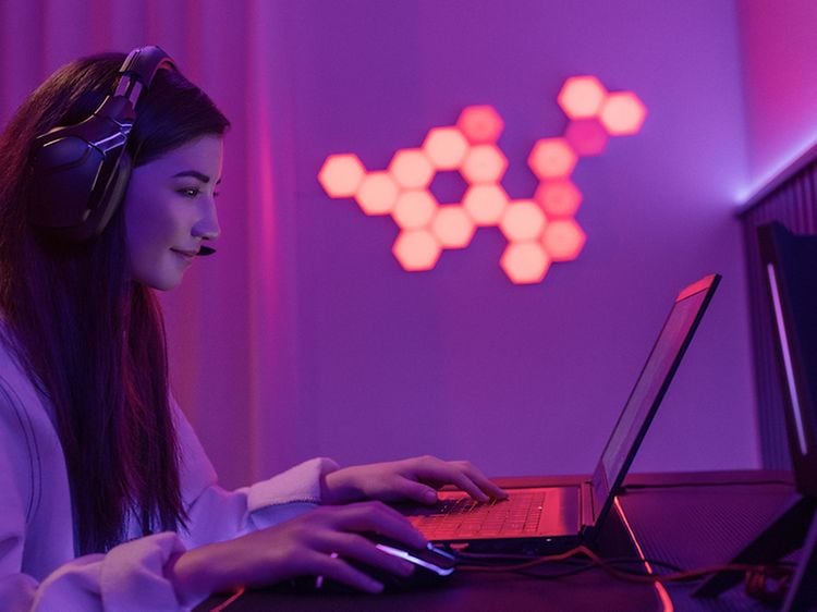 Nuori nainen istuu kuulokkeet päässään kannettavan tietokoneen ääressä pelaamassa