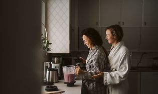 Naiset keittiössä tehosekoittimen äärellä