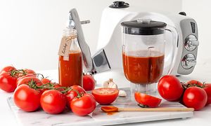 Assistant-tehosekoittimen kannussa tomaattimehua sekä tomaatteja sen ympärillä sekä Ankarsum-yleiskone taka-alalla