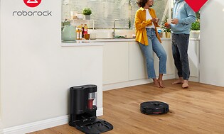 Roborock S7Max -robotti-imuri keittiön lattialla ja taka-alalla kaksi henkilöä juttelemassa keskenään
