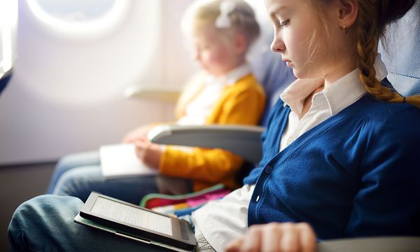 Lentokoneessa istuva nuori tyttö lukemassa e-kirjaa toisen tytön vieressä