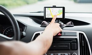 Henkilö käyttää GPS-navigaattoria autoa ajaessaan