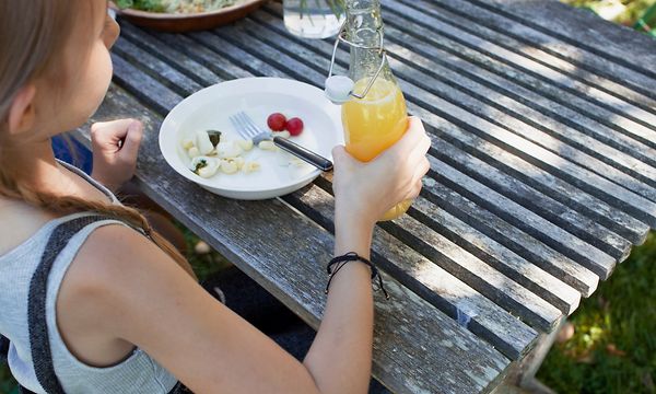Kesä - Ulkona puutarhapöydän ääressä istuva tyttö pitelee kylmää virvoitusjuomapulloa kädessään