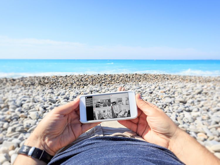 Mies makaa rannalla ja katsoo valvontakameraa älypuhelimestaan