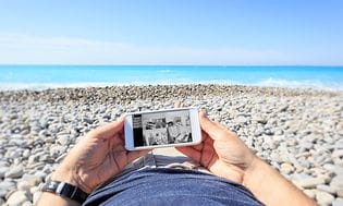 Mies makaa rannalla ja katsoo valvontakameraa älypuhelimestaan