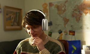 Nuori poika AirPods Max -kuulokkeet korvillaan istuessaan huoneessaan