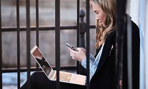 Ulkona istuva nuori nainen käyttää iphoneaan ja macbook-kannettavaansa
