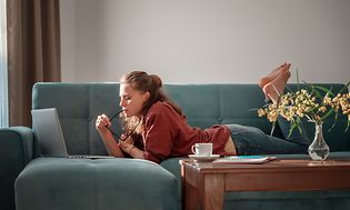 Tyttö makaa sohvalla ja käyttää kannettavaa tietokonetta