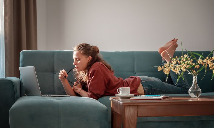 Tyttö makaa sohvalla ja käyttää kannettavaa tietokonetta