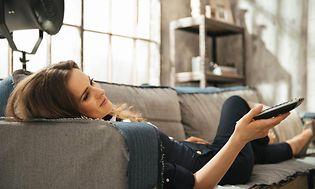 Sohvalla makaava nainen rentoutuu ja katsoo televisiota