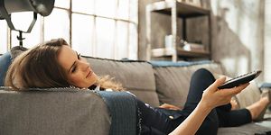 Sohvalla makaava nainen rentoutuu ja katsoo televisiota