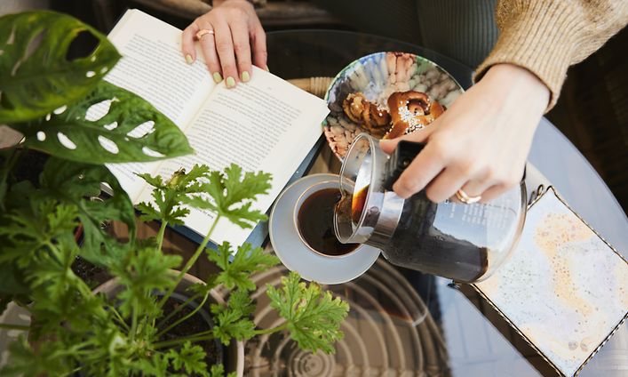 Moccamaster - Nainen kaataa kahvia kuppiin Moccamaster-kahvinkeittimen lasikannusta