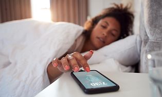 Nainen makaa sängyssä ja laittaa puhelimen herätyskellon pois päältä