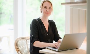 Nainen työskentelee kannettavalla tietokoneella pöydän ääressä