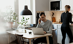 5G - Mies työskentelee kannettavalla tietokoneella ja puhuu älypuhelimellaan keittiössä