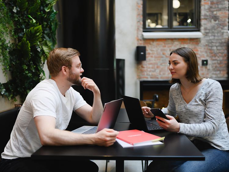 Pöydän ääressä istuva mies ja nainen työskentelevät kannettavilla tietokoneillaan