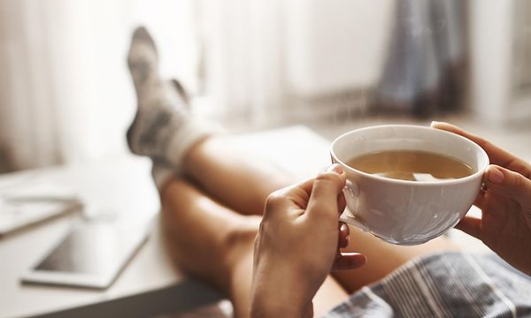 Vedenkeittimet - Istuva mies pitelee teekuppia kädessään