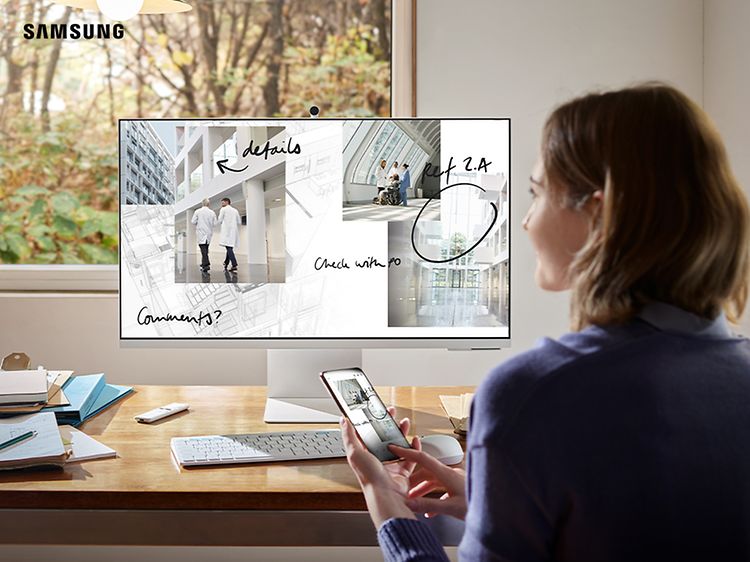 Nainen työskentelee Samsung Smart Monitor -näytöllä ja puhelimellaan, joka on yhdistetty näyttöön