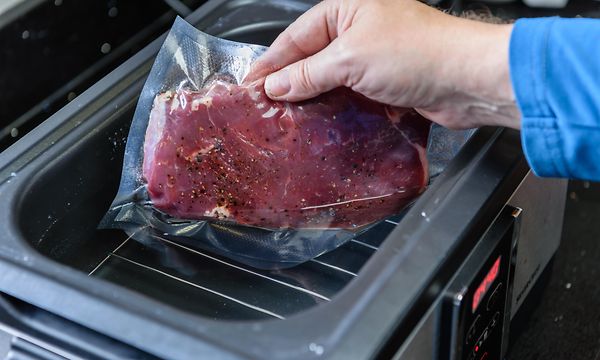 Ruoanlaitto - käsi asettamassa tyhjiöpakattua lihaa Sous Vide -laitteeseen